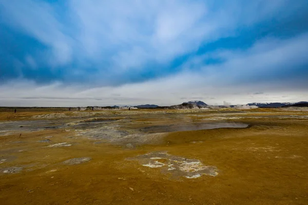 Icelandic landscape looking like on the planet Mars surface with yellow ground and blue streams. Steam is coming out of bubbling pits filled with blueish sulphate substance