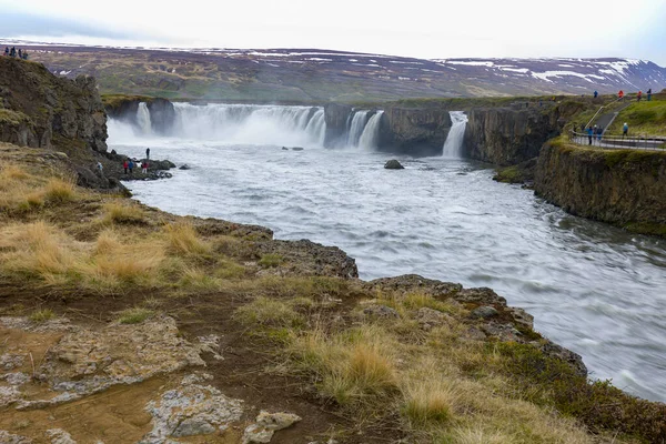 Volcanic rocks and scarce vegetations on a small hill in front of Godafoss Falls in Northern Iceland