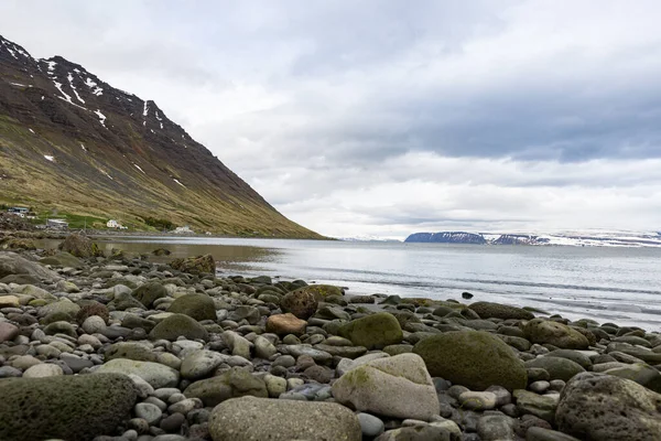 アイスランドのIsafjordur村から見られるようにフィヨルドの海岸にある岩や小石 左側の山の斜面 地平線の山脈 — ストック写真