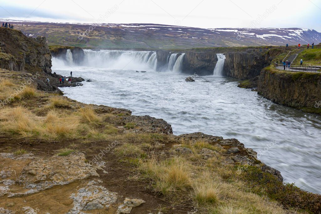 Volcanic rocks and scarce vegetations on a small hill in front of Godafoss Falls in Northern Iceland