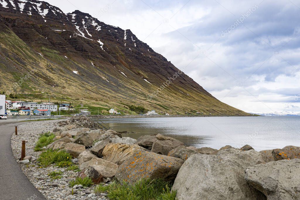 Footpath leading to houses on the slope of a mountain next to a fjord in Northern Icelandic village.