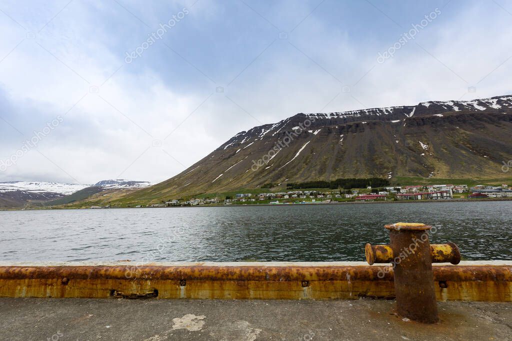 Rusted metal poll for tiding bots in a harbor in Northern Iceland with mountain range on the other side of the bay