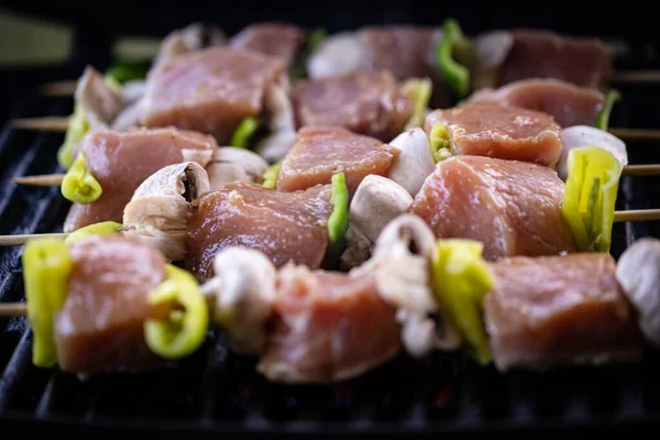 Raw pork meat, mushrooms and bell peppers skewers just placed on the barbecue.