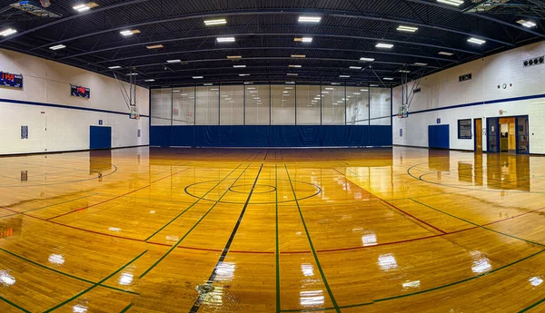 Large covered sport fields venue with courts for volleyball, basketball and badminton. Polished reflective floor reflects rows of fluorescent lights.