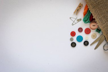 Kenevir kumaş torbasından dökülen dikiş malzemeleri. Makas, çeşitli renk izleri ve beyaz arkaplandaki düğmeler.