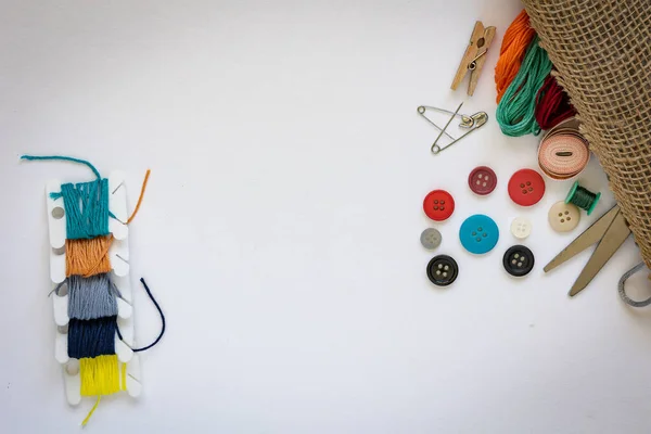 Rayon Floss treads in different colors on the left. Sewing supplies like buttons, scissors, measuring tape, stranded embroidery cotton moline, stainless steel safety pins spilling out of a fabric bag.