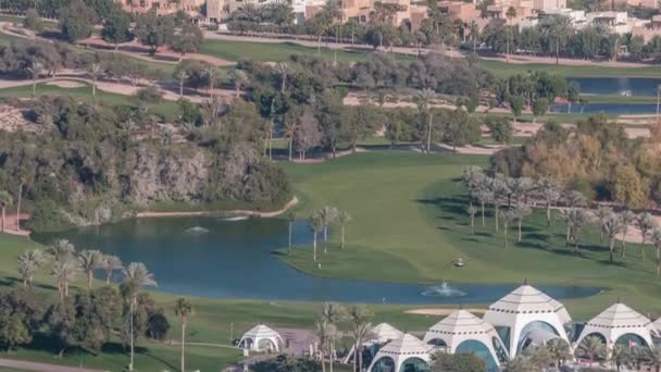 Widok z lotu ptaka na pole golfowe z zielonym trawnikiem i jeziorami, wille za nim timelapse. — Wideo stockowe