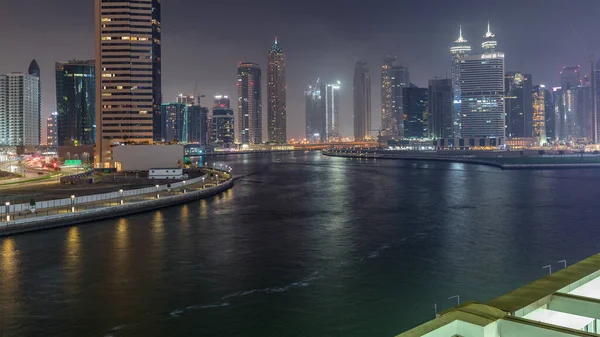 Modern city architecture in Business bay district. Panoramic aerial view of Dubai's illuminated skyscrapers reflected in water night timelapse