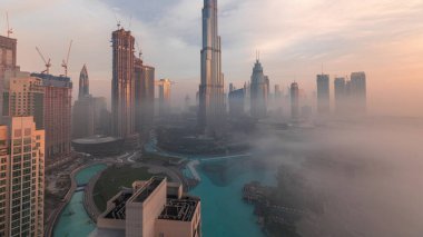 Dubai şehrinin hava panoramik görüntüsü sabahın erken saatlerinde sis zamanlarında. Gökdelenler ve gökdelenlerle dolu fütüristik şehir siluetinde gün doğumu. Güneş cam yüzeyden yansıyor