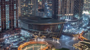 Şehir merkezinde yer alan Dubai Operası, Dubai 'de gece saatlerinde ışıl ışıl bir kültür ve sanat merkezidir. Aydınlatılmış yapay göl ve park, yukarıdan palmiye manzaralı.
