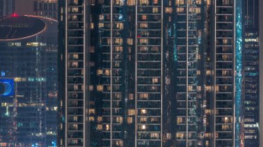 Gecenin ilerleyen saatlerinde yüksek katlı otel binasının dış tarafındaki pencereler. Zaman ayarında yanıp sönen iç ışıklar. Havadan üst görünüm