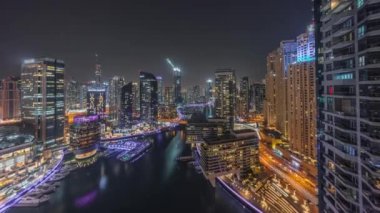 Kanal çevresindeki Dubai marina gökdelenlerine gece vakti yüzen teknelerle hava görüntüsü.