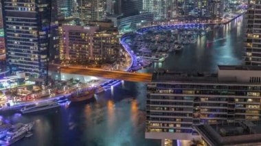 Kanal çevresindeki Dubai marina gökdelenlerine gece vakti yüzen teknelerle hava görüntüsü.