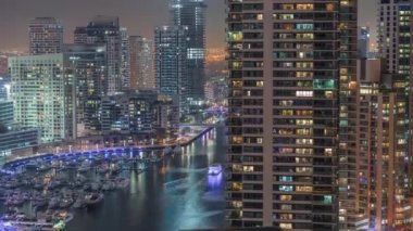 Kanal çevresindeki Dubai marina gökdelenlerine gece vakti yüzen teknelerle hava görüntüsü.
