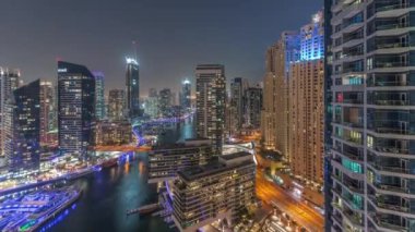 Kanal çevresindeki Dubai marina gökdelenlerine gece vakti yüzen teknelerle hava görüntüsü.
