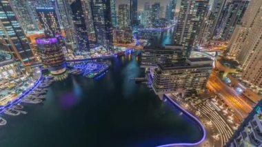 Kanal çevresindeki Dubai marina gökdelenlerine gece vakti yüzen teknelerle hava görüntüsü.