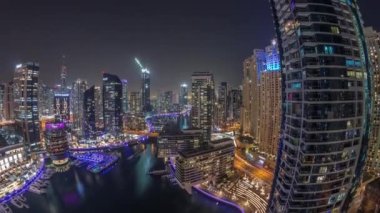 Kanal çevresindeki Dubai marina gökdelenlerine gece vakti yüzen teknelerle hava görüntüsü.