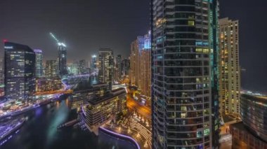 Kanal çevresindeki Dubai marina gökdelenlerine gece vakti yüzen teknelerle hava görüntüsü.