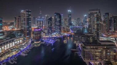 Kanal çevresindeki Dubai marina gökdelenlerine gece vakti yüzen teknelerle hava görüntüsü.
