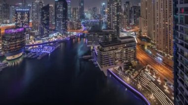 Kanal çevresindeki Dubai marina gökdelenlerine gece vakti yüzen teknelerle hava görüntüsü.