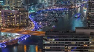 Kanal çevresindeki Dubai marina gökdelenlerine gece vakti yüzen teknelerle hava görüntüsü.