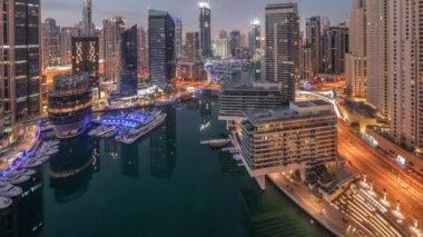 Kanal etrafındaki Dubai marina gökdelenlerine gece gündüz yüzen teknelerle hava görüntüsü.