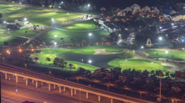 Yeşil çimenli ve göllü golf sahasına gece görüşü. Otoyolda trafik vardı. Dubai marina gökdelenlerinin manzarası.