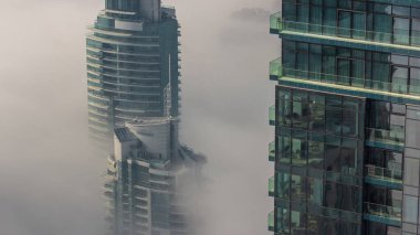 Dubai Marina ufuk çizgisi üzerinde nadir bulunan kış sisi ve hava saatleri üzerinde cam gökdelenlerle kaplı kuleler. Üst görünüm bulutların üstünde. Dubai, BAE