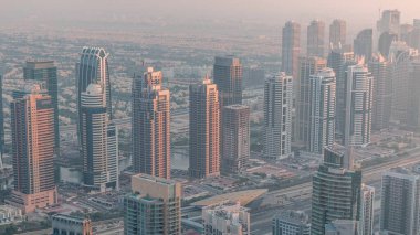 Şeyh Zayed Yolu yakınlarındaki JLT gökdelenleri ve Dubai marinası. Arkasında konut binaları ve villalar var. Gün batımında puslu bir hava