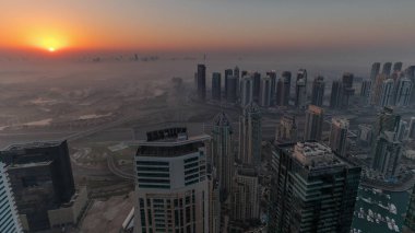 Dubai Marina Panoraması 'nda güneş doğarken JLT gökdelenleri ve golf sahası, Dubai, Birleşik Arap Emirlikleri. Yukarıdan hava manzarası sisli bir sabah. Turuncu gökyüzü ile şehir silueti