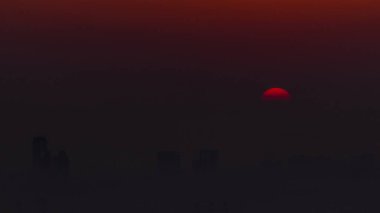 Sabah Dubai ufuk çizgisinde gün doğumu yakın görüntüsü, Dubai marinası zaman çizelgesinden gökyüzü görüntüsü. Turuncu gökyüzündeki büyük güneş gökdelenlerin etrafındaki sislerin üzerinde yükseliyor. Birleşik Arap Emirlikleri