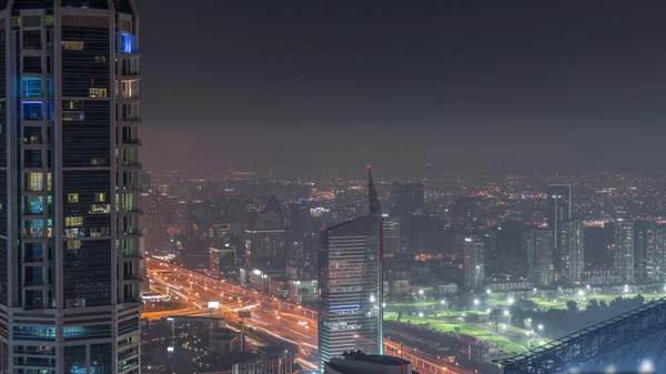 ドバイの空の景色は ドバイのマリーナから夜のバーシャの高さと緑の地区のエリアの時間経過を示しています ライトアップされた塔や高層ビルが建ち並び 上から高速道路を走っています — ストック写真