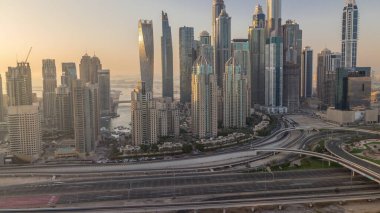 Dubai Marina karayolu kavşağı spagetti kavşağı akşam saat dilimi. Cam bir yüzeye batan güneşi yansıtan en uzun gökdelenler. Gün batımında JLT bölgesinden hava görüntüsü