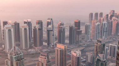 Güneş doğarken Şeyh Zayed Yolu yakınlarındaki JLT gökdelenleri ve marina kuleleri. Konut binaları ve villalı ufuk çizgisi. Sıcak turuncu ışıkla gün doğumunda sisli bir sabah