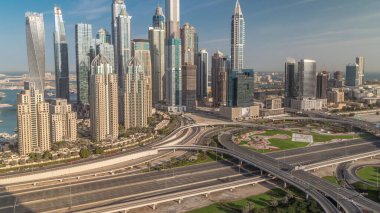 Dubai Marina karayolu kavşağı spagetti kavşağı zaman dilimi. Arka plandaki en uzun gökdelenler. JLT bölgesinden sabah hava görüntüsü. Bulutlu gökyüzü