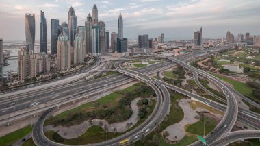 Dubai Marina karayolu kavşağındaki panorama spagetti kavşağı günden geceye geçiş zamanı. Gün batımından sonra en uzun gökdelenler ve arka planda golf sopası. JLT bölgesinden hava üst görünümü.