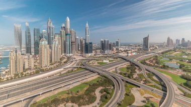 Dubai Marina karayolu kavşağındaki panorama spagetti kavşağı tüm gün boyunca devam etti. Arka planda hızla hareket eden gölgeli en uzun gökdelenler. JLT bölgesinden hava görüntüsü. Bulutlu gökyüzü