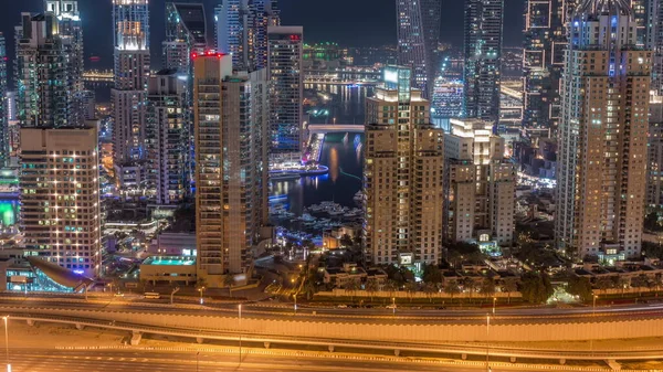 Dubai Marina 'nın gökdelenleri tüm gece boyunca en yüksek konut binalarıyla aydınlandı. Tekneli su kanalı ve camları yanıp sönen ışıklar. JLT bölgesinden hava üst görünümü