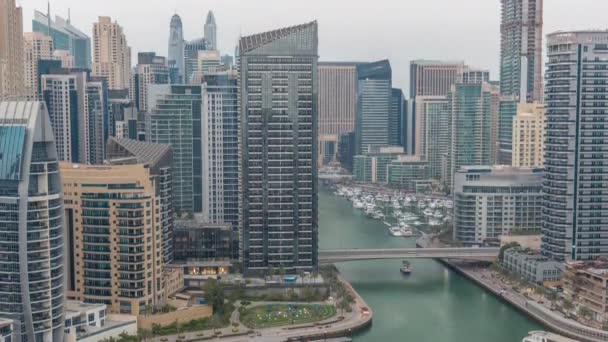 Dubai Marina con varios barcos y yates estacionados en el puerto y rascacielos alrededor del canal aéreo día a noche timelapse. — Vídeo de stock