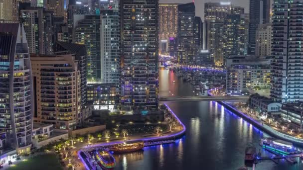 Dubai Marina avec plusieurs bateaux et yachts garés dans le port et gratte-ciel autour du canal timelapse de nuit aérienne. — Video