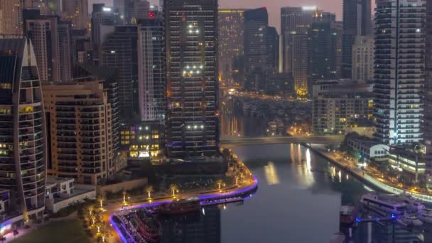 Dubai Marina with several boats and yachts parked in harbor and skyscrapers around canal aerial night to day timelapse. — Stock Video