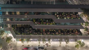 Açık havada, gece vakti açık havada rahat bir restoranın havadan görünüşü. Dubai 'nin finans bölgesinde masalarda oturan insanlar. Otomobiller girişe yakın.