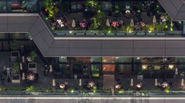Açık havada, gece vakti açık havada rahat bir restoranın havadan görünüşü. İnsanlar Dubai 'nin finans bölgesinde masalarda oturuyor.