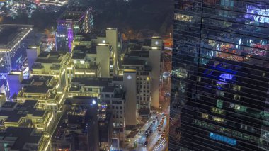 Dubai 'nin finans bölgesindeki oteller ve ofis binaları. Gökdelende parlayan pencereler ve cephede akşam aydınlatması. Caddelerde trafik