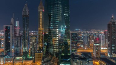 Dubai 'nin finans merkezi, gece gündüz aydınlık lüks gökdelenler geçiş zamanı, Dubai, Birleşik Arap Emirlikleri. Pencerelerde ve ofis kulelerinde ışık olan hava manzarası
