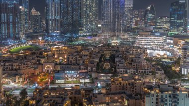 Gökdelenlerle çevrili eski kasaba adasının aydınlatılmış geleneksel evlerinin gökdelenlerle dolu gece manzarası. Dubai şehir merkezinde alışveriş merkezi ve çarşıya yakın çeşme alanı var.