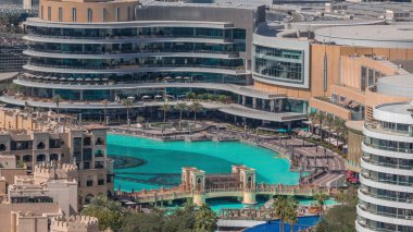 Alışveriş merkezinin dış tarafında Dubai şehir merkezindeki havadan zaman ayarlı fıskiyeler var. Birleşik Arap Emirlikleri. Göl üzerinde köprü ve palmiyelerle yürüme alanı