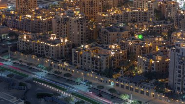 Gökyüzü manzarası, eski kasaba adasının aydınlatılmış geleneksel evlerini yukarıdan görüyor. Dubai şehir merkezinde alışveriş merkezi ve çarşıya yakın çeşme alanı var. Ağaçları ve trafiği olan cadde