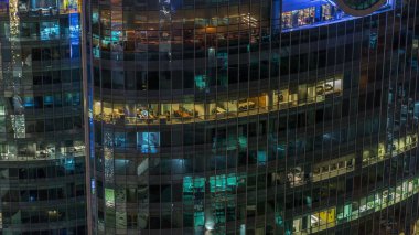 Modern ofisteki büyük parlayan pencereler ve konut binaları gece saatlerine göre ayarlanıyor, pencereler ışık saçıyor. Finans bölgesinde gökdelenler