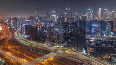 Dubai 'nin modern mimarisine sahip Skyline, karayolu trafiğiyle gece kulelerini aydınlattı. Kanal ve şantiyeli hava panoramik görüntüsü